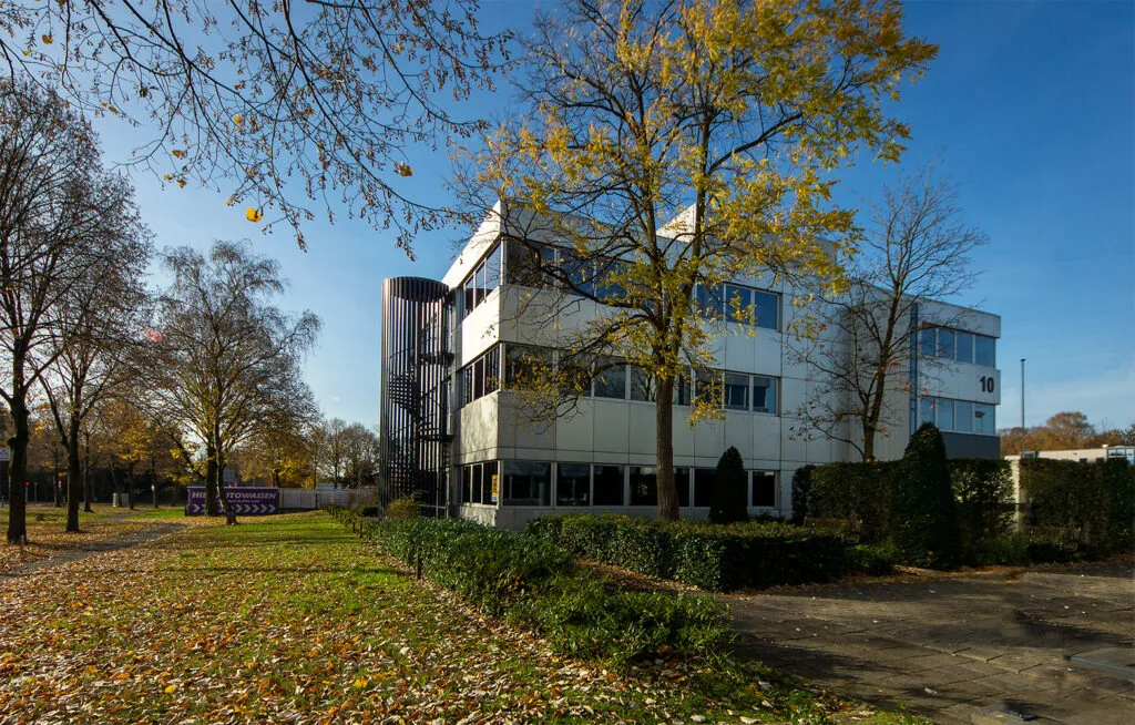 Kantoorpand aan de Huis ter Heideweg in een groene omgeving met herfstbladeren op de grond.